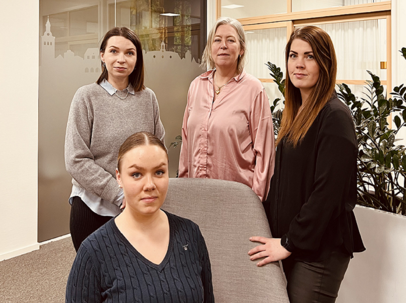 Tre personer står bakom en fotölj. En person sitter i fotöljen.